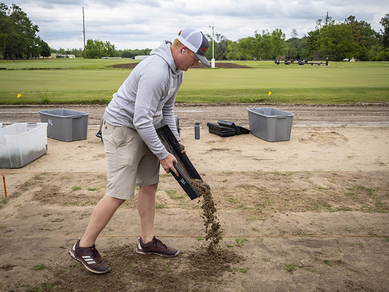 A graduate student pouring soil at the turfgrass fields.
