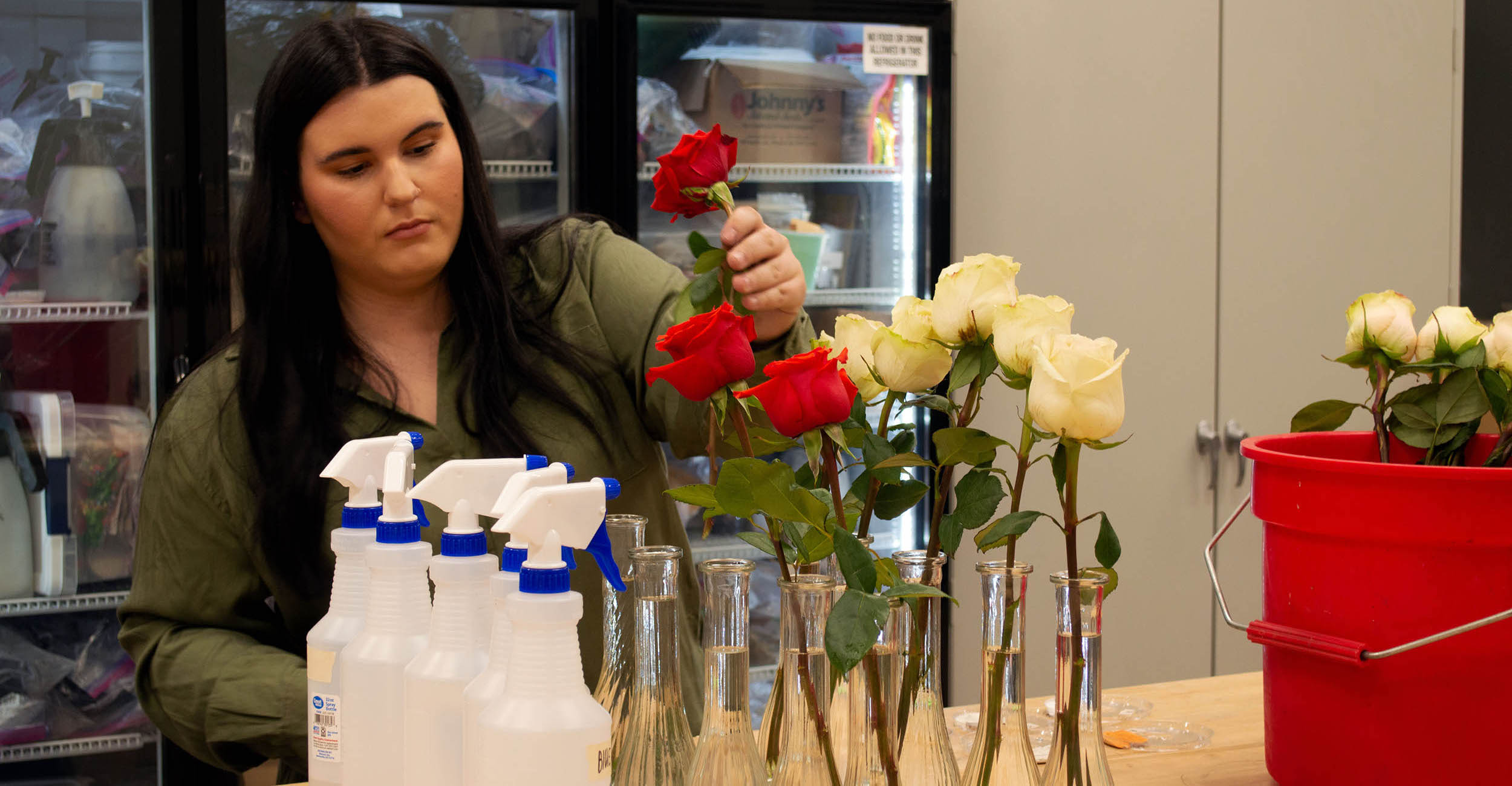 2023-flower-research-banner.jpg Abby Pace placing roses into vases on a counter top.